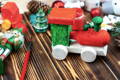 A festive wooden toy train painted in red, green, and white sits on a rustic wooden table, surrounded by Christmas decorations, a nutcracker figurine, and painting supplies.