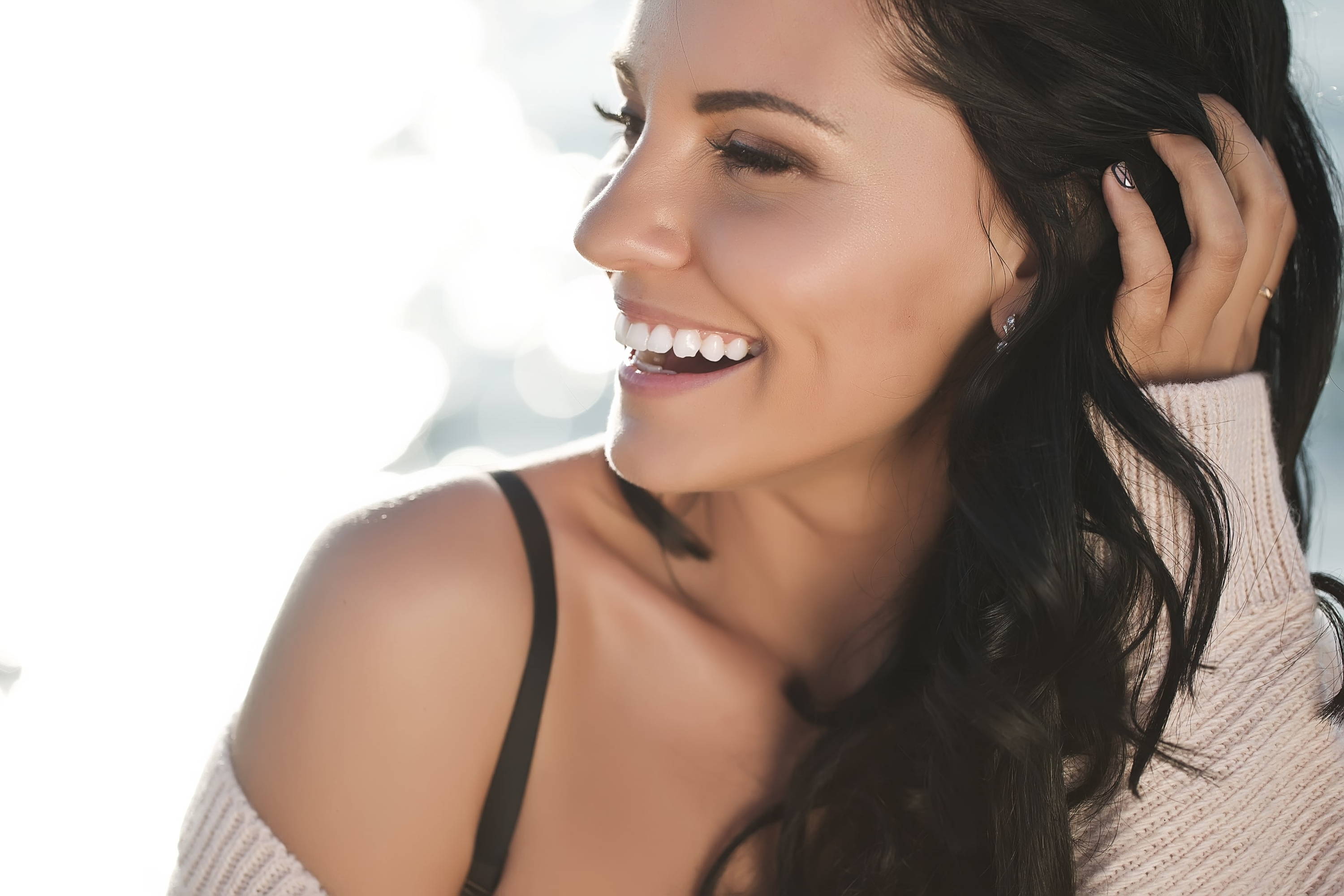 woman with dark hair smiling and holding her hair back 