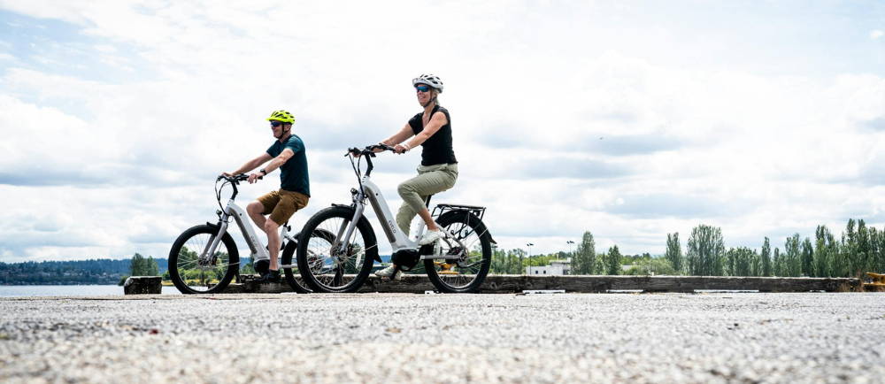 Two riders on electric bikes next to lake