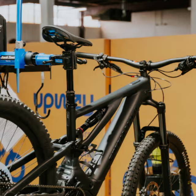 a full suspension electric mountain bike on a stand in front of Upway bloxes as an upway center
