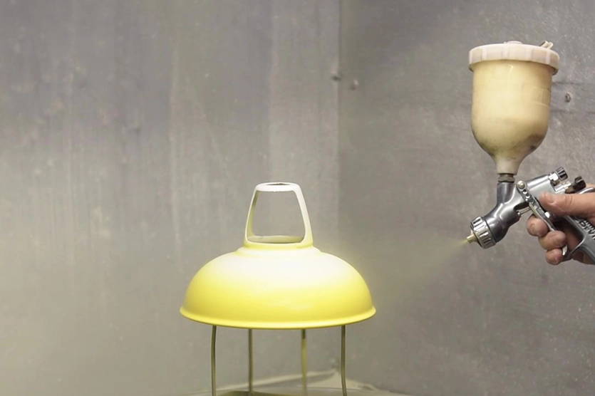 A person spraying yellow liquid vitreous enamel in the outside of a Coolicon shade