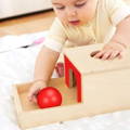 Baby boy holding a red ball while playing with a wooden Montessori toy on a blanket. 