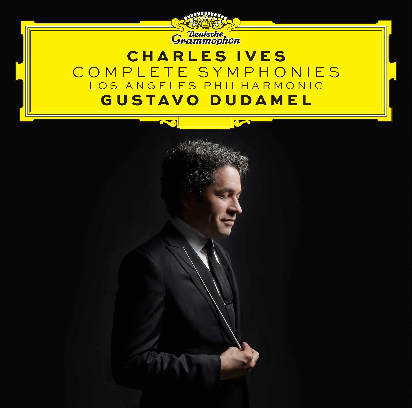 Portada del álbum de Ives: Sinfonías Completas. Perfil lateral de Gustavo Dudamel  sobre un fondo negro mirando hacia abajo, sonriendo, sosteniendo su batuta. Sobre su cabeza, "Charles Ives, Complete Symphonies, Los Angeles Philharmonic, Gustavo Dudamel " en un cuadro de texto amarillo de Deutsche Grammophon.