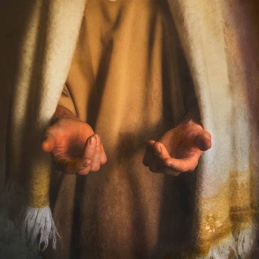 Upclose picture of Jesus's hands turned palms up. Gold and cream robe in the backdrop.