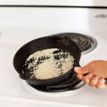 A cast iron skillet over a white stove top is filled with sesame seeds which are being toasted