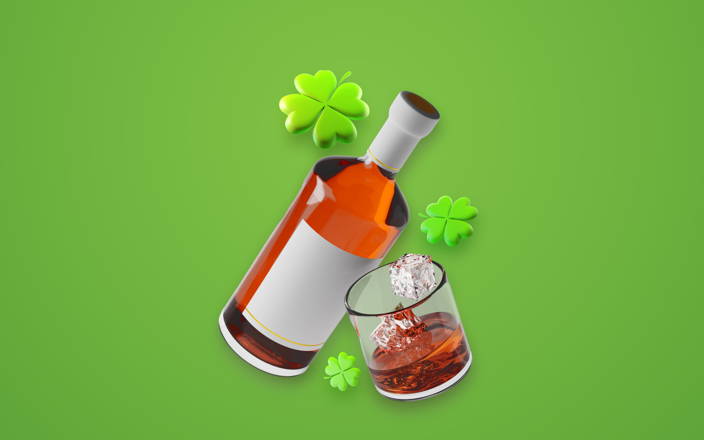 Bottle of Irish whiskey, glass of whiskey with ice, and four leaf clovers against a green background (preview)