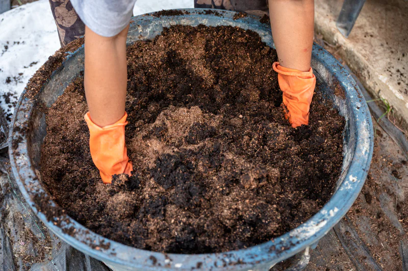 A large bucket of compost being turned over by hand