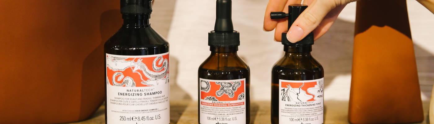 Davines ENERGIZING products displayed in a line with a hand reaching for the Thickening Tonic