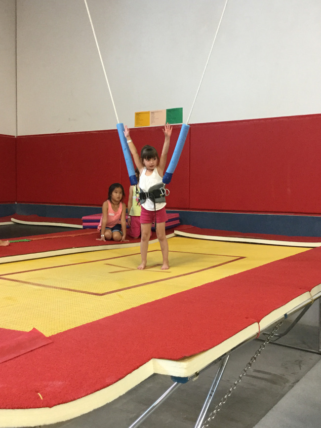 Little girl gets ready to do a tumble with bungee support during gymnastics class