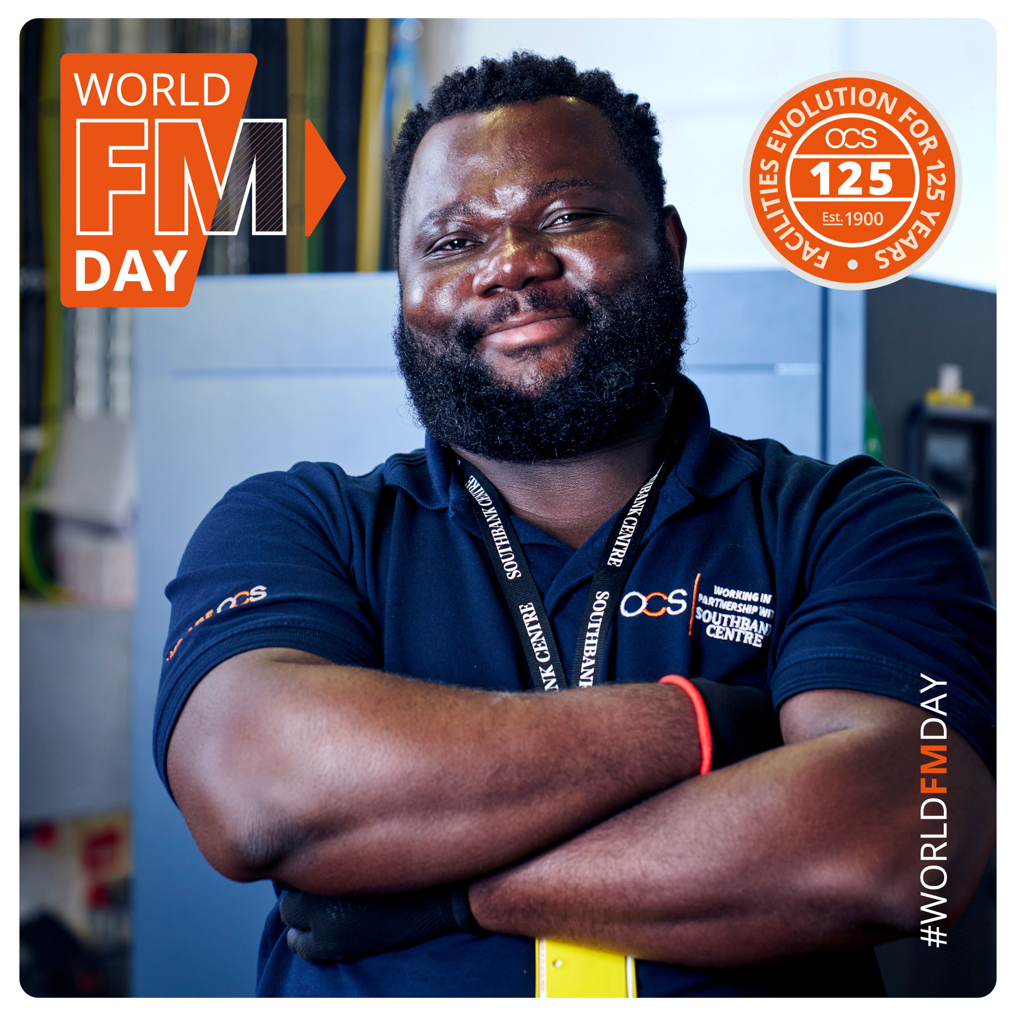 A smiling man with folded arms wearing a black OCS lanyard and navy uniform stands in a workspace. Text reads World FM Day and OCS 125 Years, with the hashtag #WORLDFMDAY in the corner.