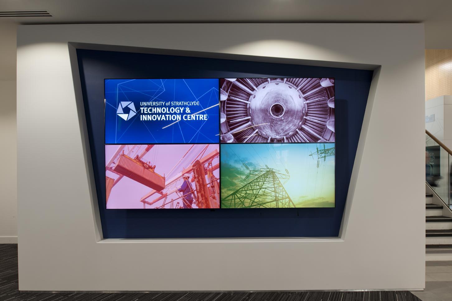 A display screen on a wall shows four images: University of Strathclyde Technology & Innovation Centre logo, a jet engine close-up, industrial equipment, and an electricity pylon with wires.