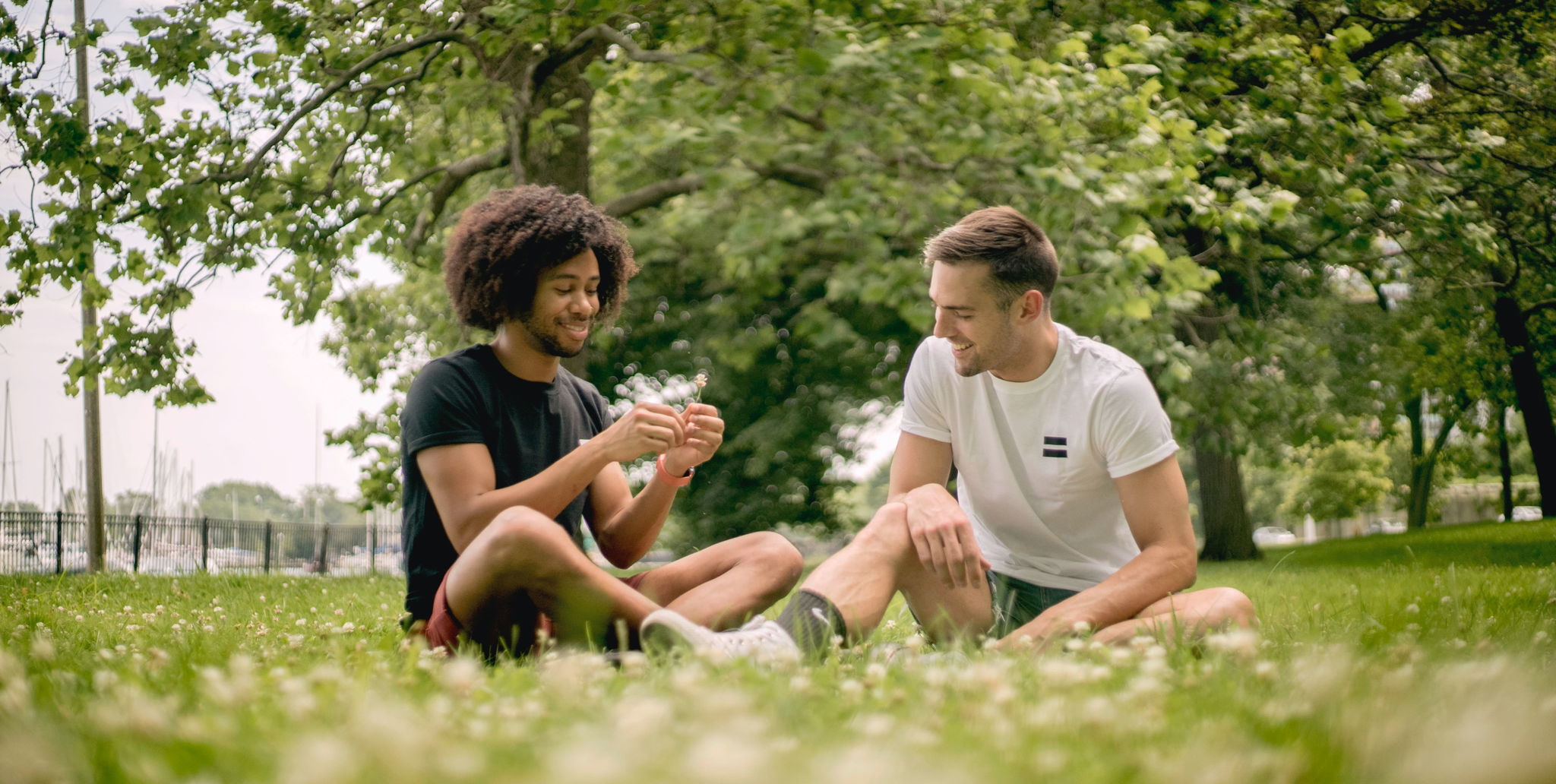 A pair of guy friends wearing shorts and shirts playing card games and laughing together.