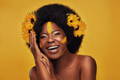 African american woman with sunflowers in naturally curvy hair and painted face against yellow background
