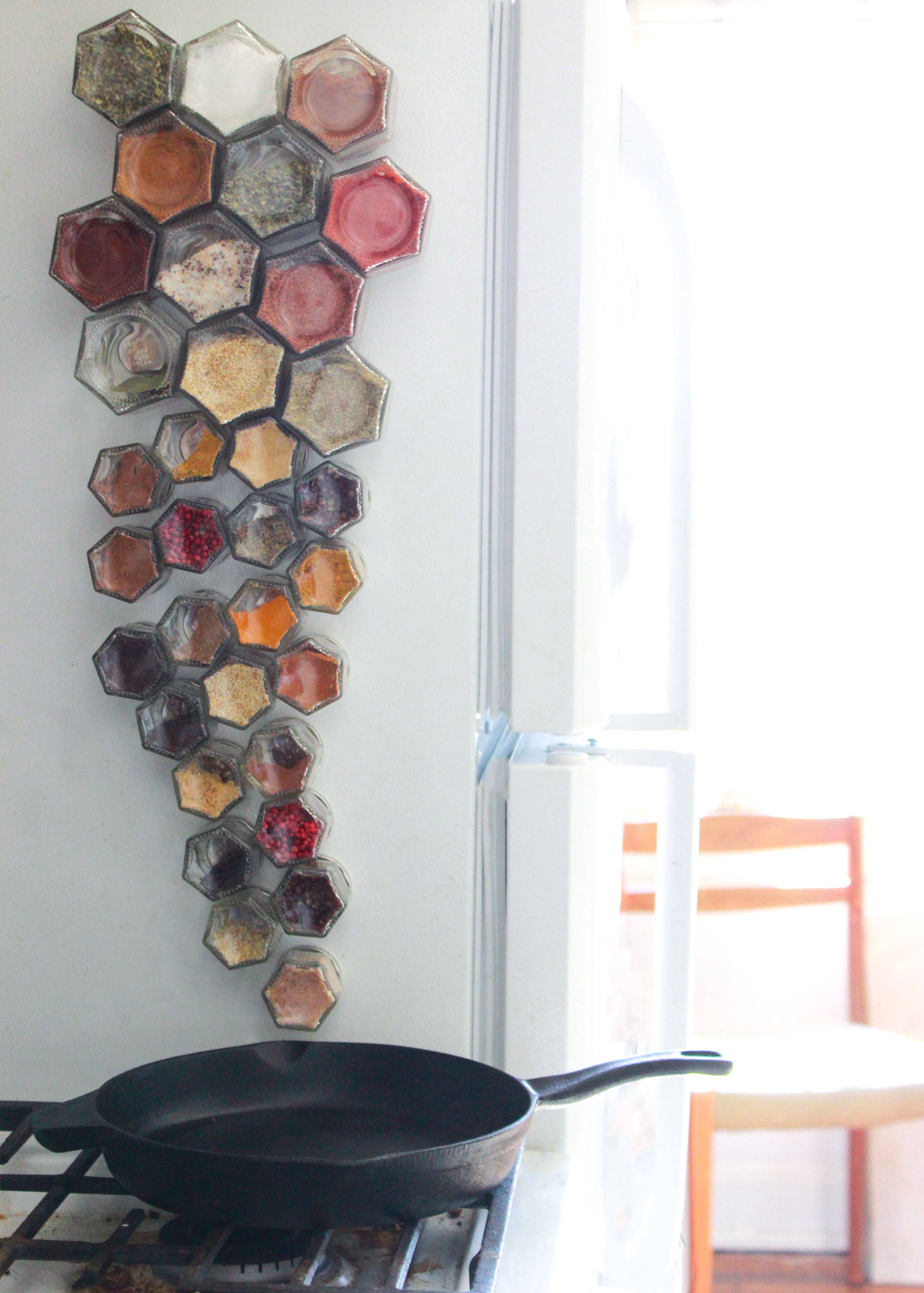 A vertical group of glass spice jars positioned from larger to smaller leading down to a cast iron skillet