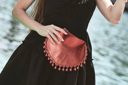 CHARMAINE red leather clutch bag with tonal pearl charms, worn with a black dress.