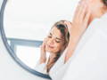 woman touching her face and looking in the mirror