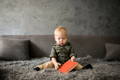 Baby sitting on a grey sofa and holding a red book.