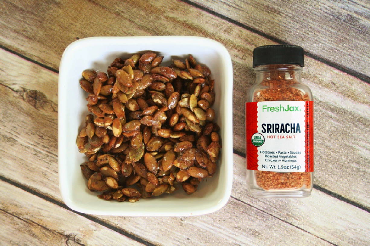 A bottle of FreshJax Sriracha Hot Sea Salt next to a bowl of sriracha pumpkin seeds. 