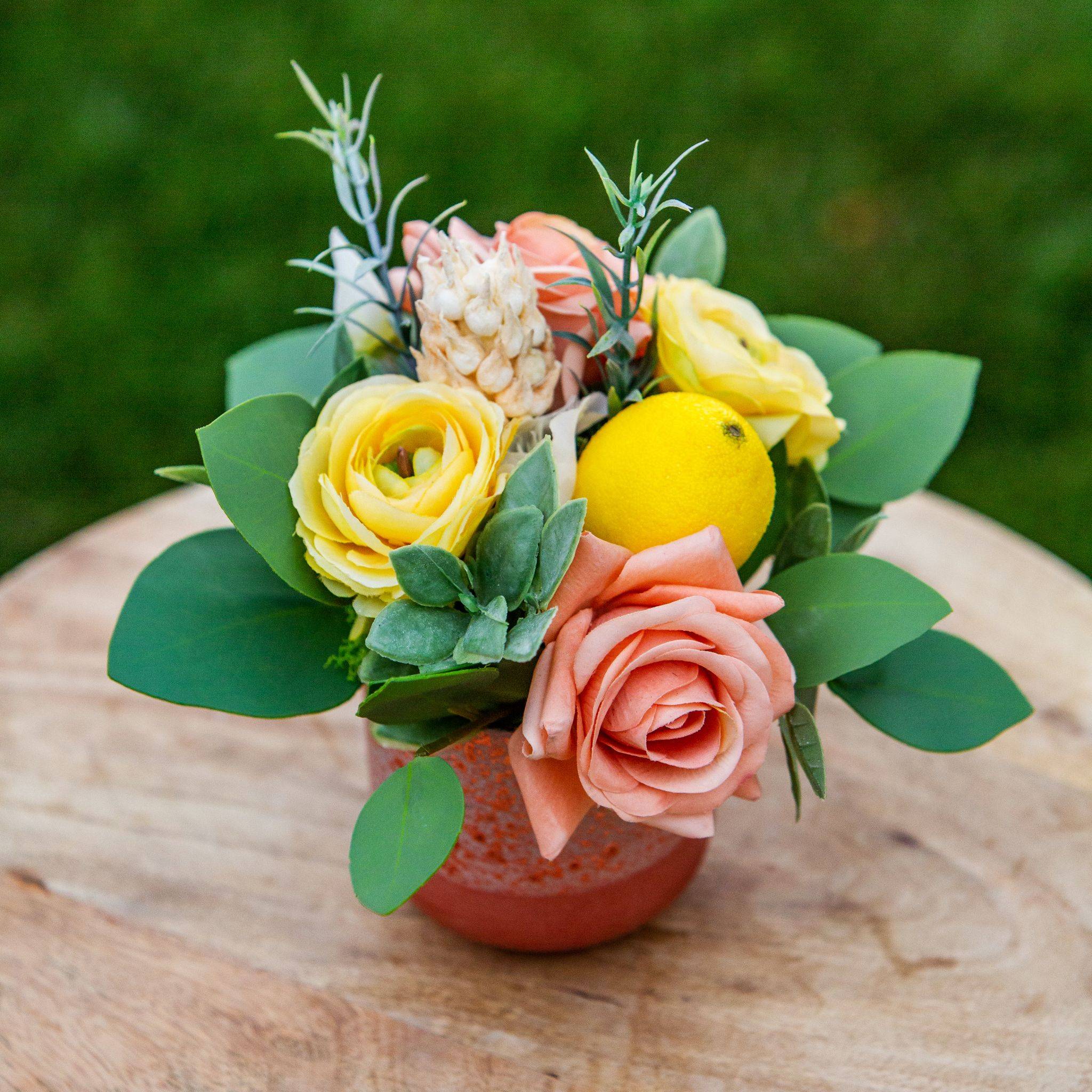A small centerpiece with peach roses, yellow ranunculus, coral peonies, lemons, gumdrop eucalyptus, and boxwood
