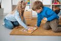 Brother and sister playing with a wooden Montessori toy on the carpet in their playroom.