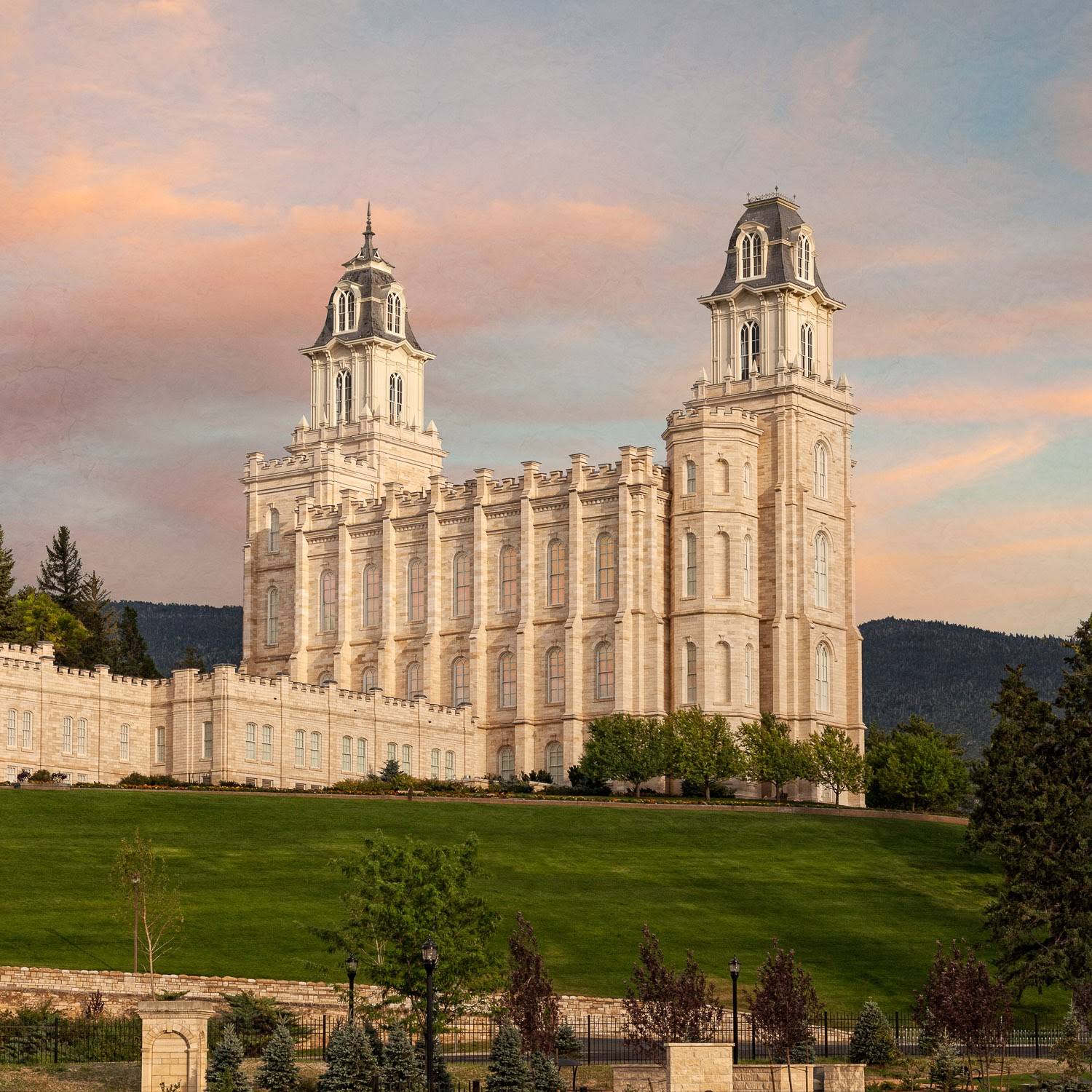 Photo of the Manti Utah Temple standing on a green hill against a pastel sky.