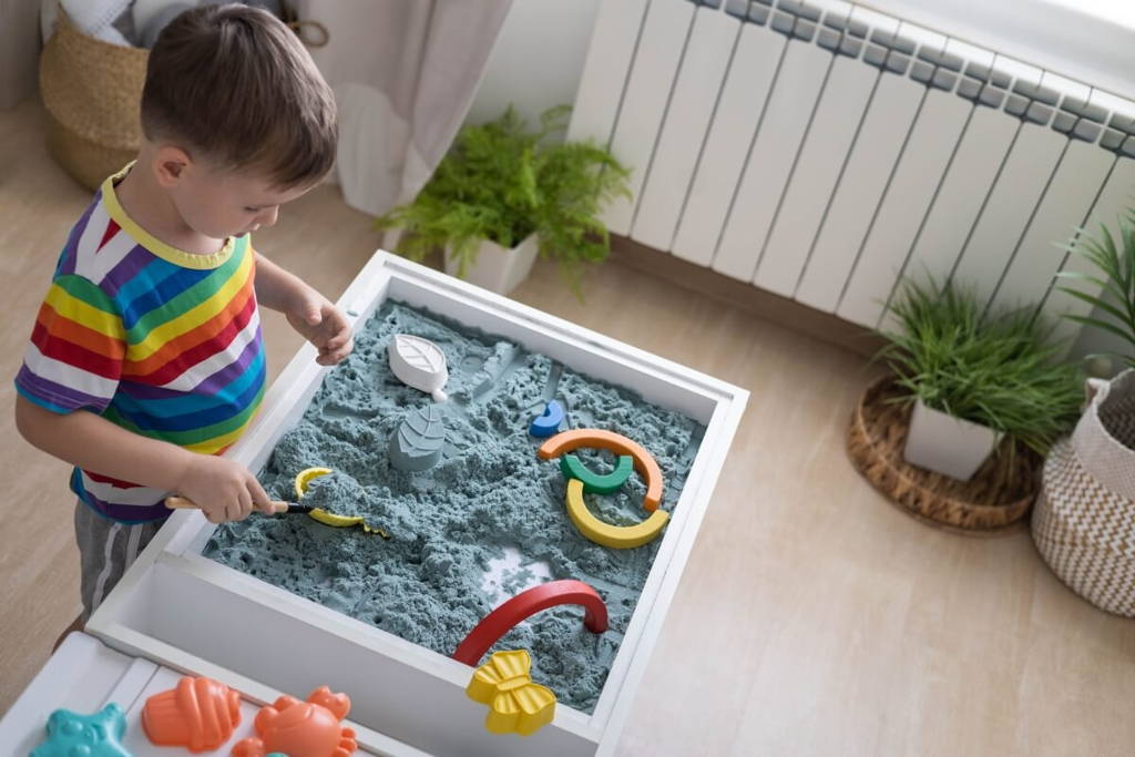 Boy playing with a sensory table filled with blue sand and toys.