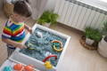 Boy playing with a sensory table filled with blue sand and toys.