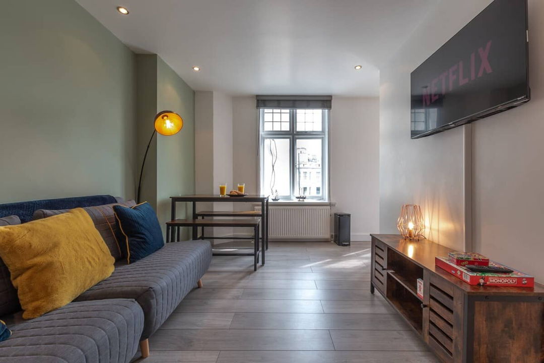 Living room with sofa and large TV, dining table at the far end by the window