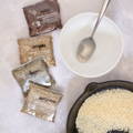 Four plastic spice pouches labeled 'Organic Seasoning' and the name of the spice it contains lay next to a white ceramic bowl and skillet full of sesame seeds