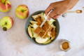 A dark blue bowl is filled with sliced apples as cinnamon is being poured over the top