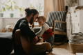 Father playing the guitar while his baby is touching the strings.