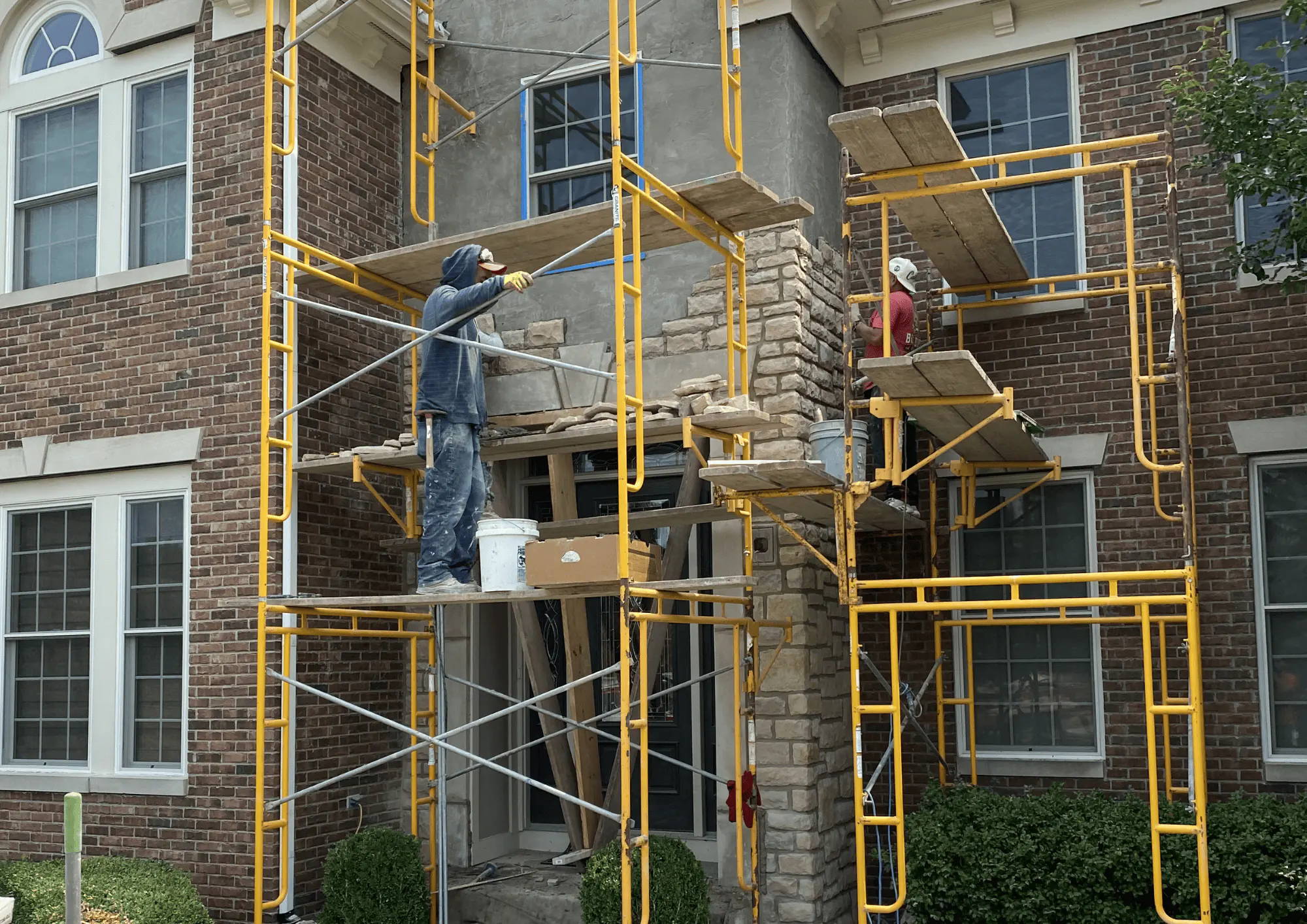 Scaffolding in front of a red brick building where repair work is being performed above two windows.
