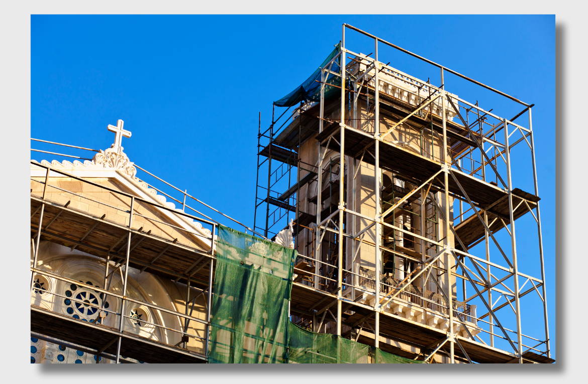 Historic church undergoing masonry restoration, with scaffolding surrounding the bell tower and facade under a clear blue sky.