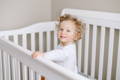 Little boy inside his white crib. 