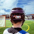 Player on field wearing maroon lacrosse helmet with Tozuda indicator attached to back of helmet.
