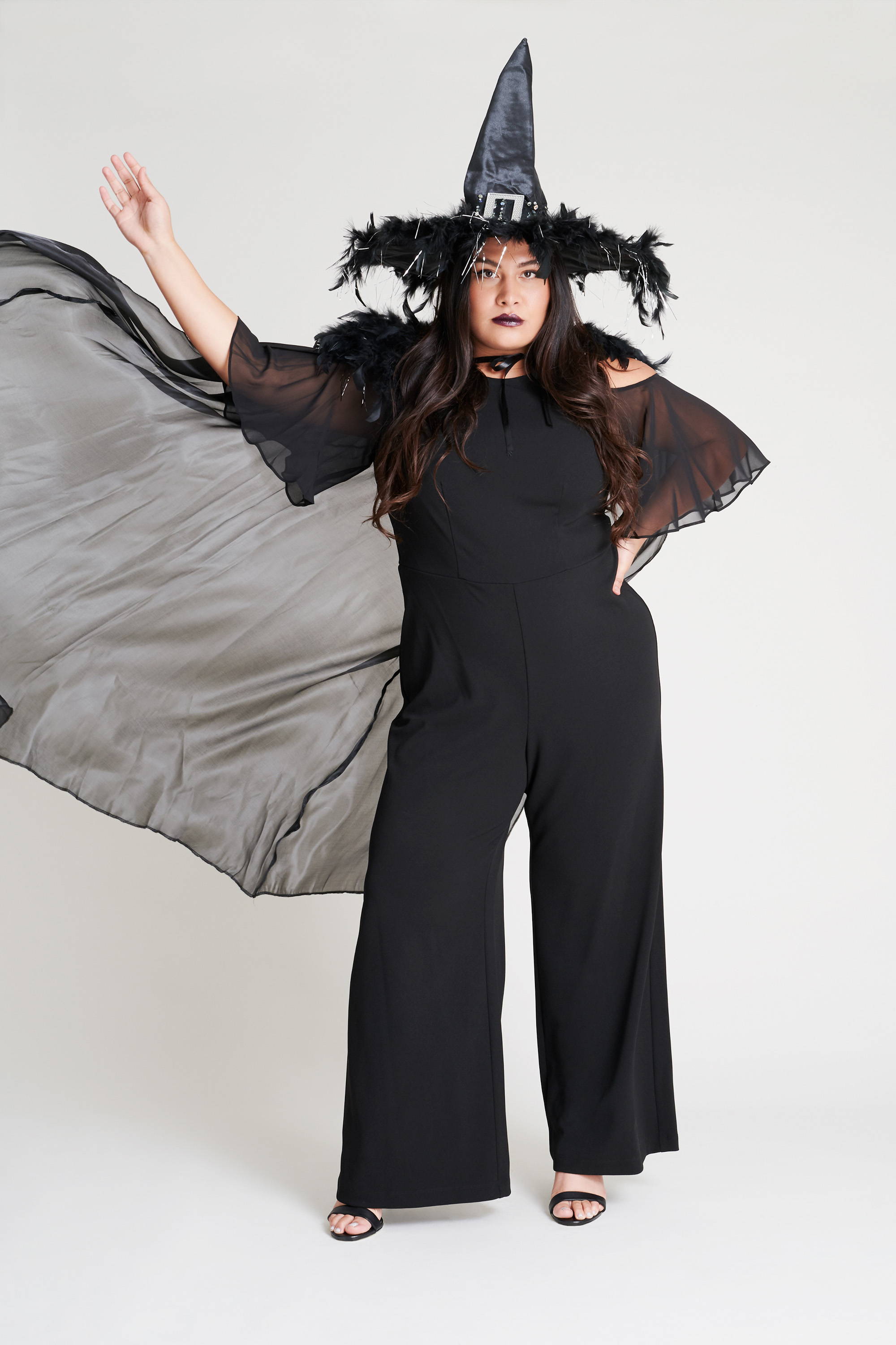plus size woman in black cold shoulder jumpsuit and witch hat on diy halloween costumes connected apparel blog
