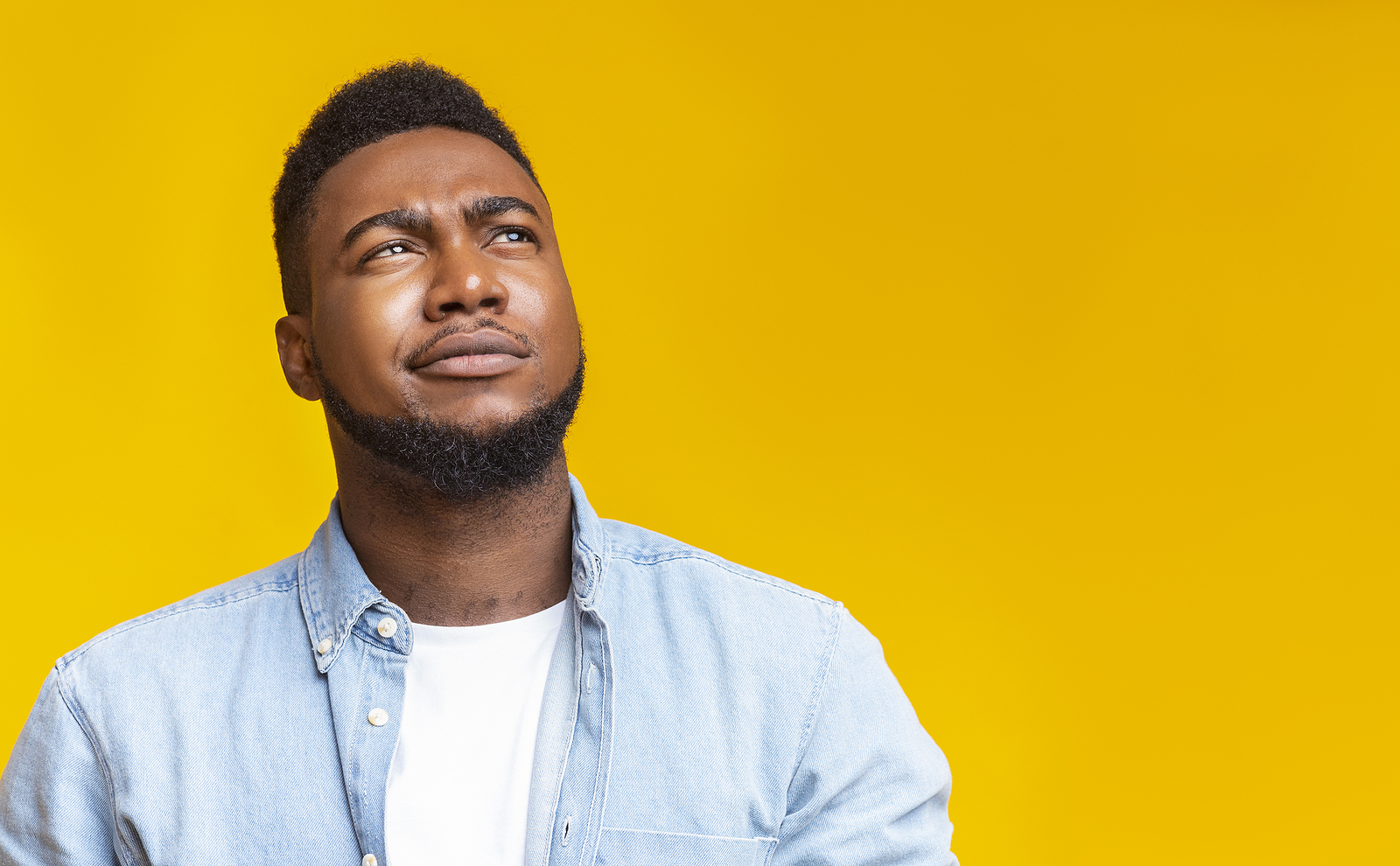 A black man looks up while making a confused expression.