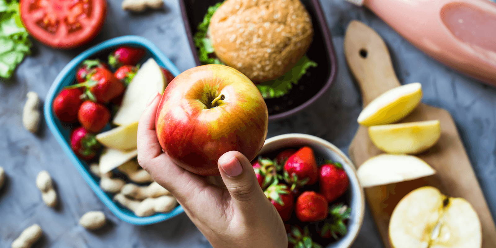 Person holding an apple in front of a table of food.