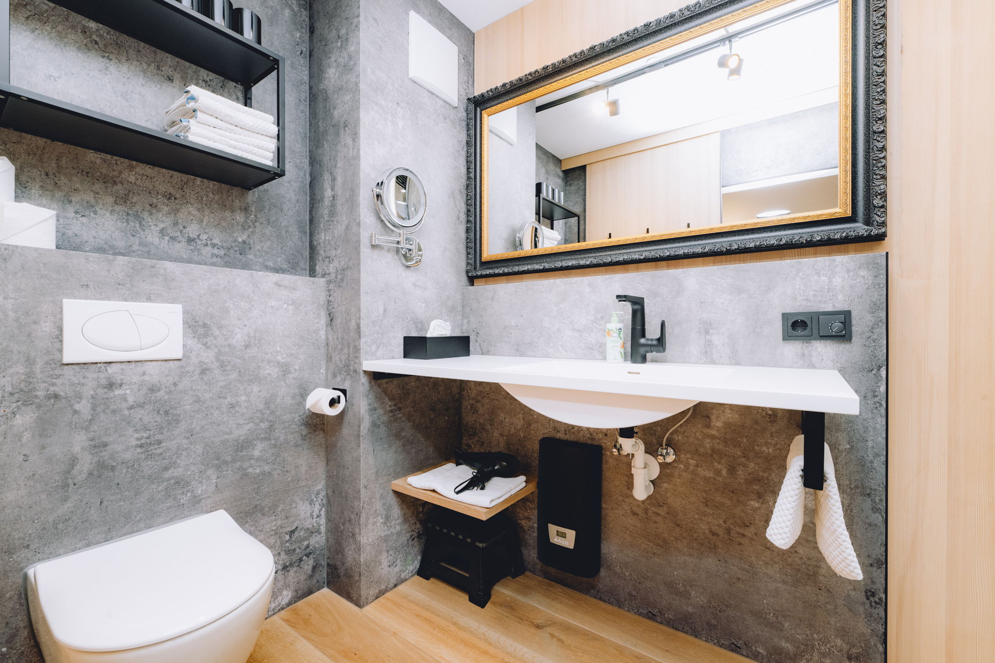 Ein modernes Badezimmer mit Steinwänden, Holzboden und einem dunkel gerahmten Spiegel.