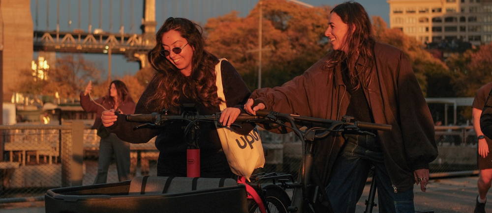2 happy females on e-bikes ar sunset in a city