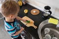 Little boy slicing a cucumber in the kitchen.