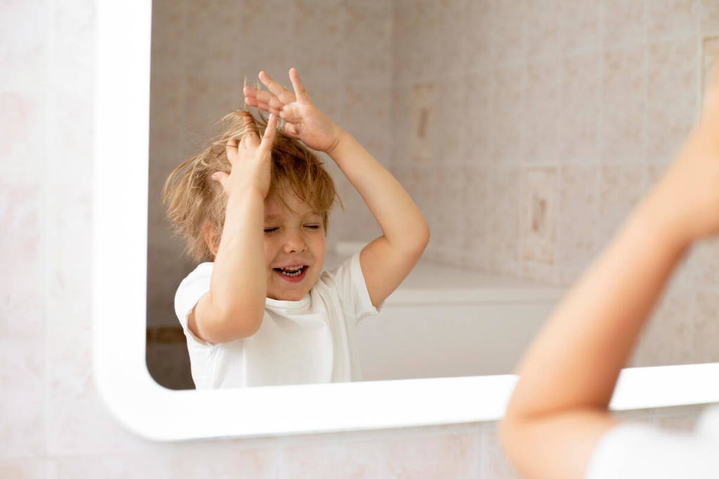 Toddler fixing his hair will standing in front of a mirror.