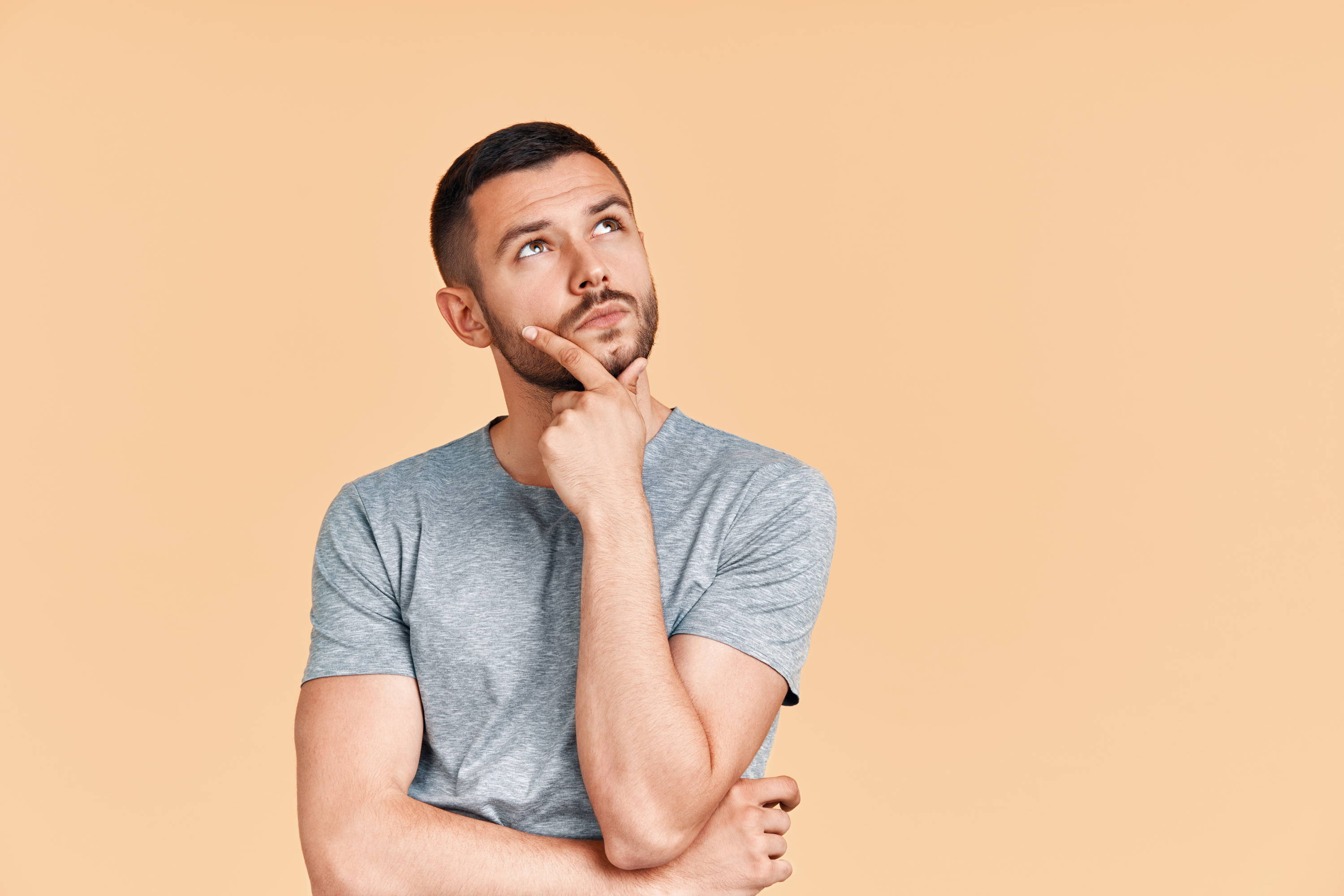 Man with beard looking up in thoughtful pose with beige background