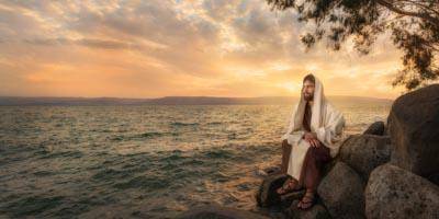 Jesus sitting on rocks by the seashore.