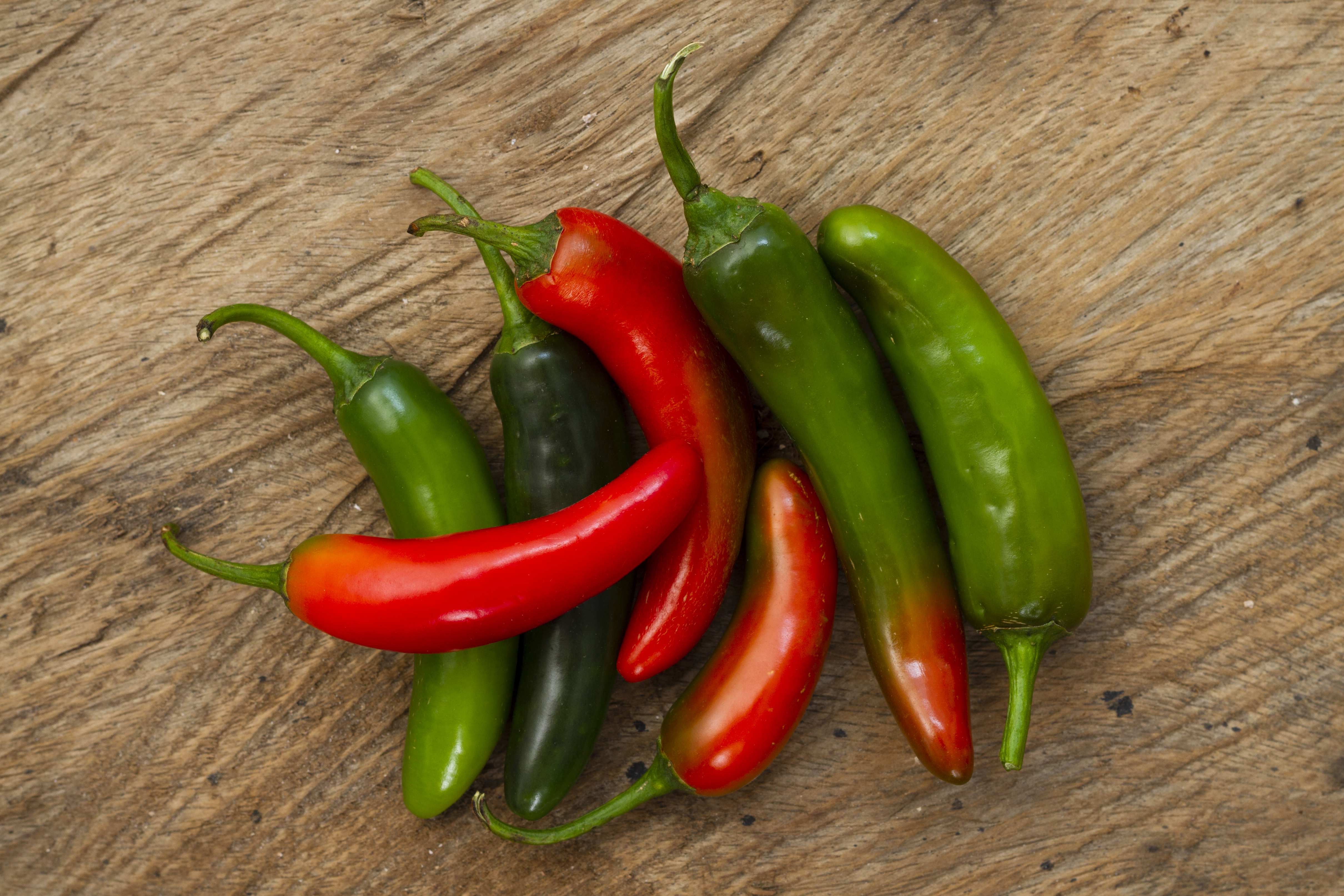 Green and red serrano peppers on a wooden background