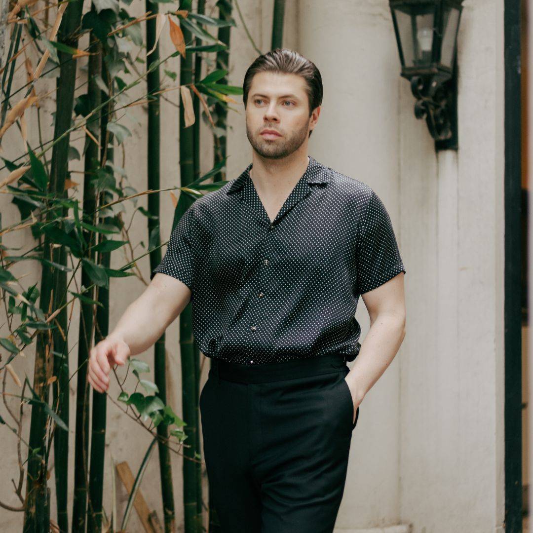 model walking outside while wearing black pants and a short sleeve black dotted silk shirt from 1000 kingdoms