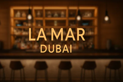 LA MAR DUBAI text over a blurred warm image of a bar interior featuring shelves of drinks, hanging lights, and empty stools.