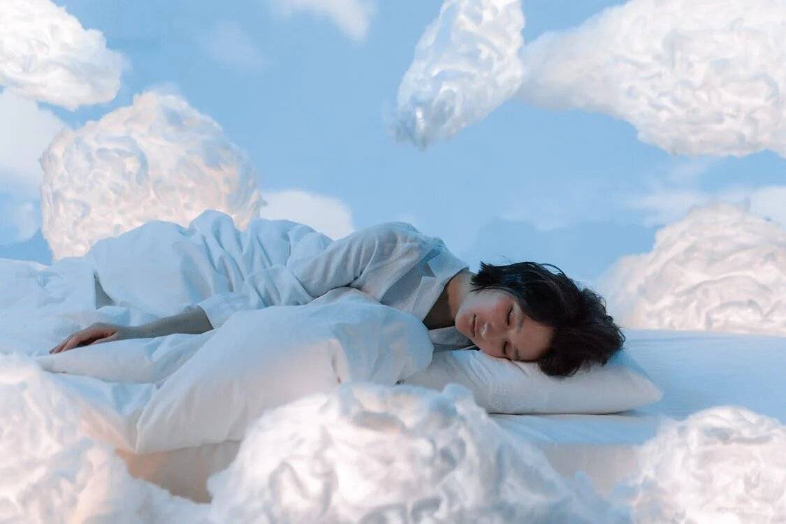 Lady dreaming of sleeplng on clouds while snuggling under soft and luxurious duvet