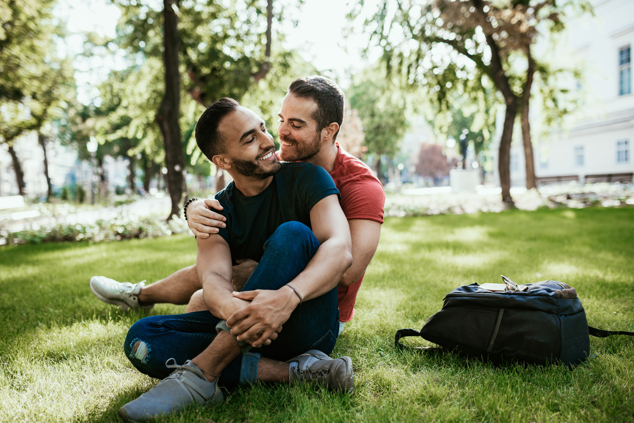 An attractive male couple wearing jeans and t-shirts, hold eachother at a park.