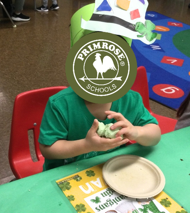 primrose student playing with green sensory dough wearing a leprechaun hat